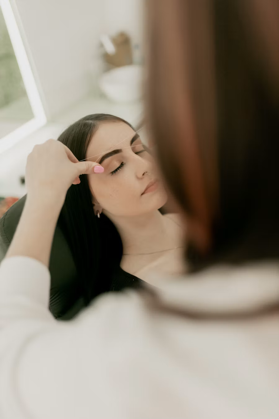 A brow artist shaping a client's eyebrows in a bright studio